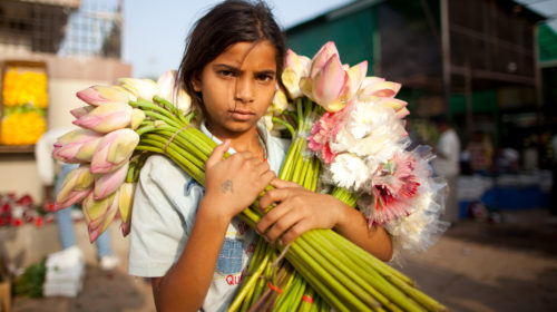 lavoro minorile e bambini al lavoro, bambina indiana venditrice di fiori fotografata all'alba