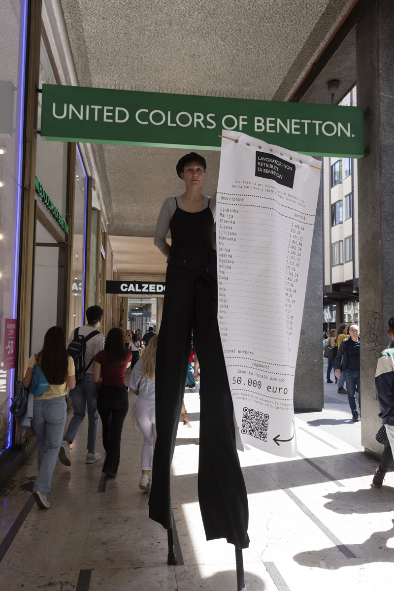 Trampoliera con uno scontrino gigante "Lavoratori non retribuiti di Benetton" davanti al negozio di Milano. Importo totale: 50mila euro