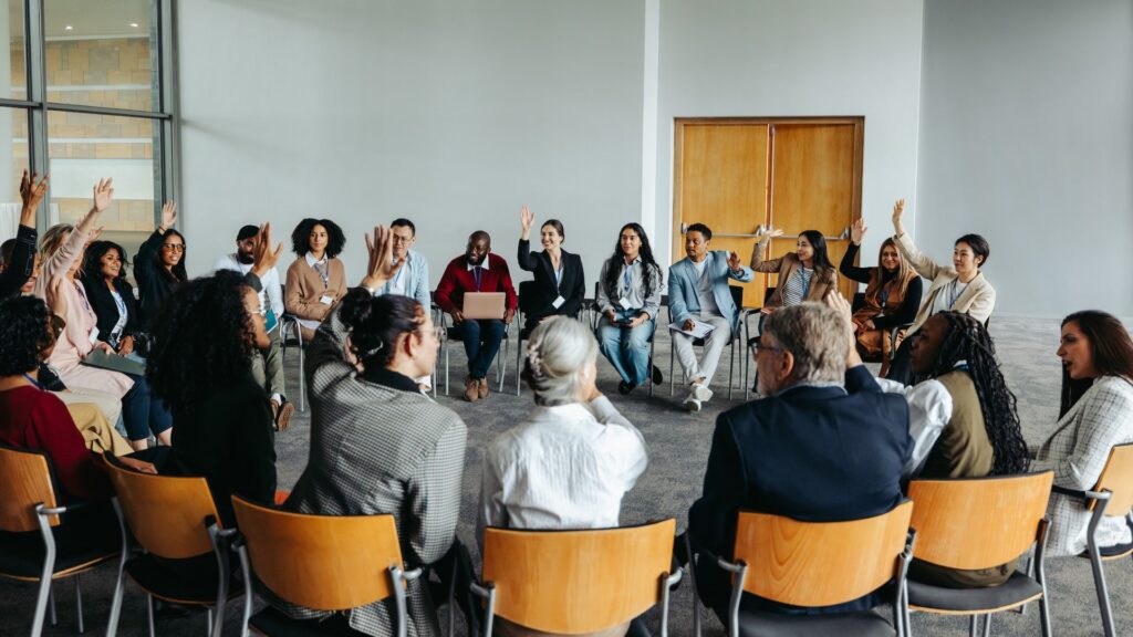 Persone sedute in cerchio durante un'assemblea alzano la mano per votare