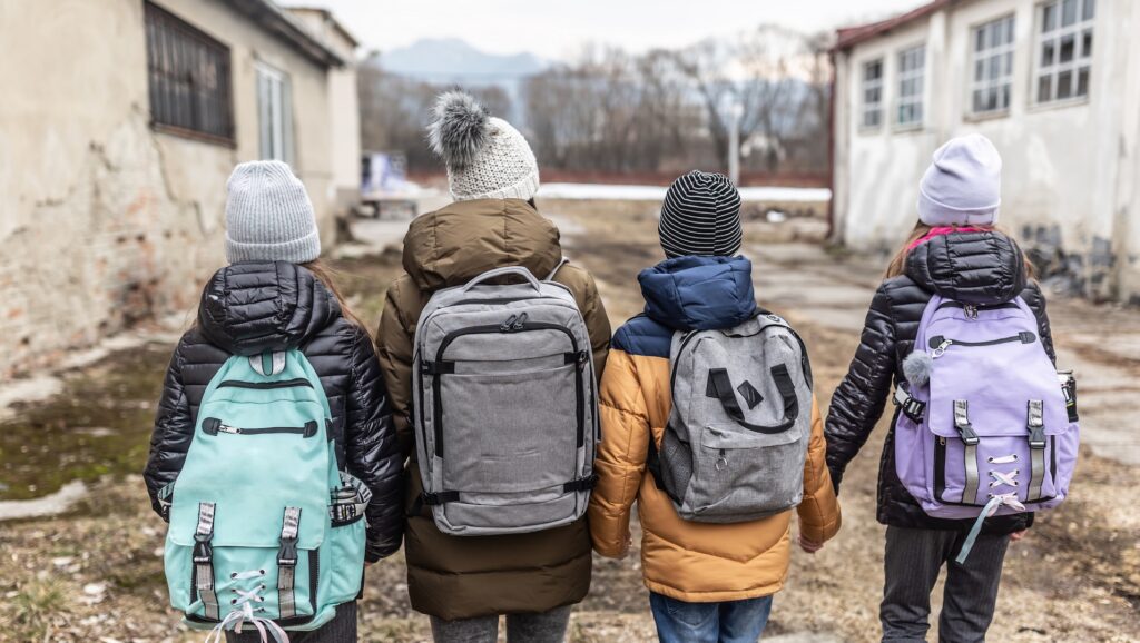 Quattro bambini di spalle con zaini diretti a scuola: la spesa sociale rischia di essere ridotta a causa dell'aumento della spesa militare