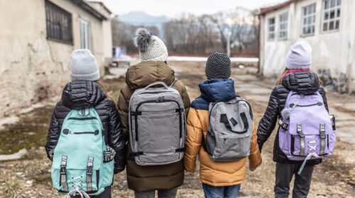 Quattro bambini di spalle con zaini diretti a scuola: la spesa sociale rischia di essere ridotta a causa dell'aumento della spesa militare