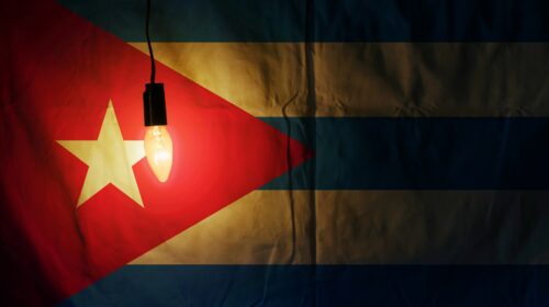 Bandiera di Cuba illuminata da una lampadina appesa a un filo, su sfondo in penombra