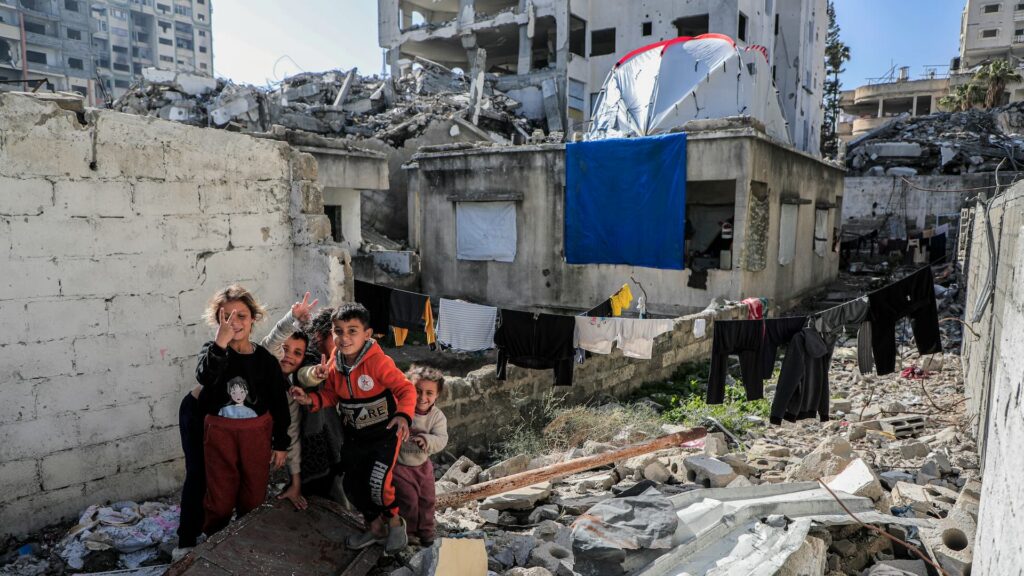 Bambini sorridono tra le macerie di edifici bombardati a Gaza