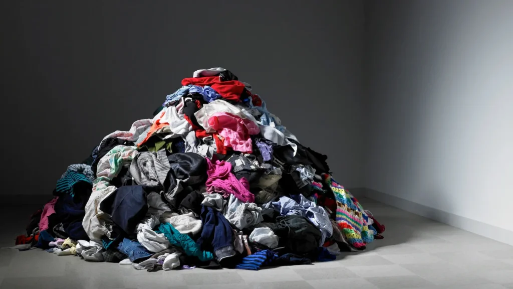 Mucchio di vestiti ammassati sul pavimento di una stanza vuota, simbolo dell'invenduto della moda