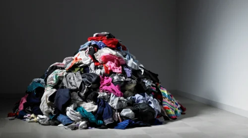 Mucchio di vestiti ammassati sul pavimento di una stanza vuota, simbolo dell'invenduto della moda