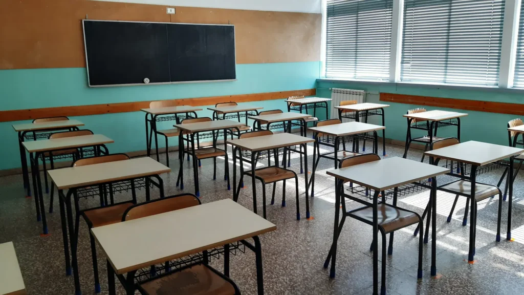Aula scolastica italiana con banchi vuoti e vecchio radiatore, persiane abbassate