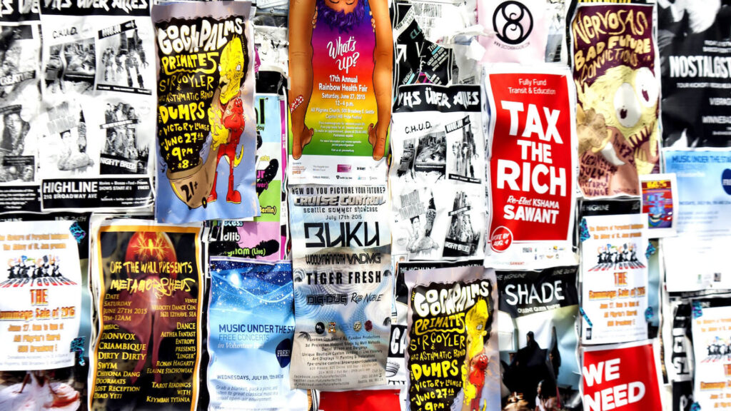 Manifesto 'Tax the rich' tra i poster di un muro urbano, simbolo della tassa sui patrimoni dei miliardari