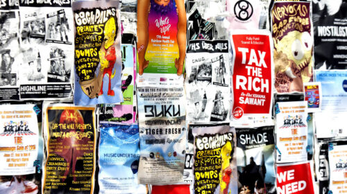 Manifesto 'Tax the rich' tra i poster di un muro urbano, simbolo della tassa sui patrimoni dei miliardari