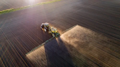 Trattore che spruzza pesticidi su un campo, inquinamento da modello di sviluppo agricolo