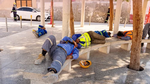 Operai edili in tuta da lavoro riposano all’ombra su una panchina durante un’ondata di caldo