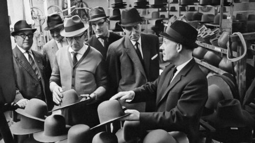 Foto d'archivio in bianco e nero di uomini in abito e cappello di feltro che provano cappelli in un negozio
